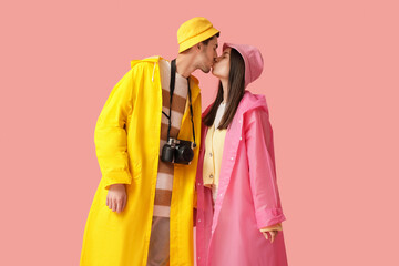 Wall Mural - Young couple in raincoats kissing on pink background