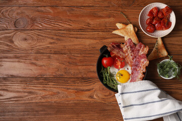 Wall Mural - Frying pan with fried egg, bacon and tomatoes on wooden background. Top view