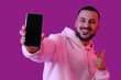© Pixel-Shot - Young man pointing at blank mobile phone on violet background, closeup