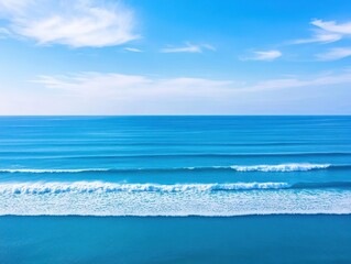 Poster - Aerial View of Tranquil Ocean Waves Lapping Gently Against Rocky Shoreline Under Bright Blue Sky with Fluffy White Clouds Creating a Serene Atmosphere