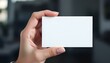 © peja - A hand holding a blank white card, close-up focus, with a blurred professional background, creating a clean and minimalistic look.