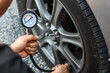 © Eakrin - Hand car mechanic holding car tire pressure check equipment tool to checking low tire pressure inflating tires to or refill or air inflate to safety and car care service maintenance inspection.
