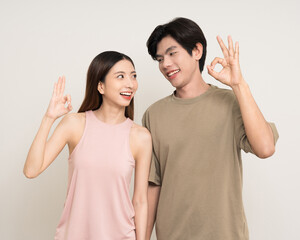 Wall Mural - Ok Happy asian couple attractive in various action gesture standing on isolated white background. Cheerful Smiling young man and woman showing ok sign