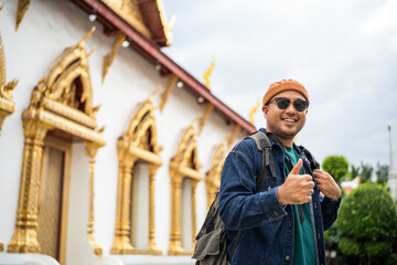 Young Asian traveling backpacker walking in temple at Bangkok Thailand. Happy tourist walking in the downtown street traditional ancient temple. Holiday vacation time tourist