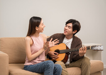 Wall Mural - Happy moment of asian family man and woman husband and wife just married buying new house. Relax playing guitar on sofa in living room