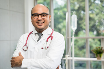 Asian doctor standing posing work from hospital. Positive male physician with stethoscope in hospital background. Healthcare and medical concept.