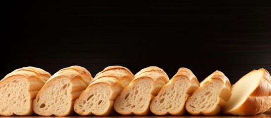Poster - Sliced French bread on a dark background with warm light highlighting the crust, arranged neatly for breakfast with ample copy space.