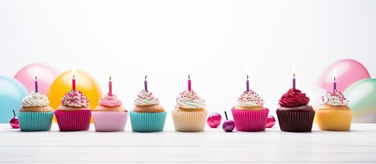 Poster - Colorful row of cupcakes with candles on white background, featuring pink, blue, beige, purple, and chocolate frosting, complemented by pastel balloons.