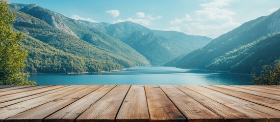 Poster - Scenic view from empty wooden tabletop featuring serene blue lake and majestic green mountains under a clear sky creating a tranquil atmosphere