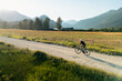 © Cavan Images - Cyclist pedalling on a dirt road with fields and mountains around