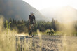 © Cavan Images - Biker on a gravel road in a sunlit rural landscape by mountains.