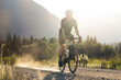 © Cavan Images - Cyclist on a gravel road in a sunlit rural landscape by mountains.