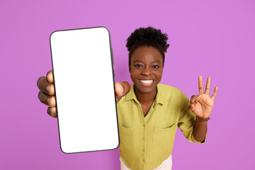 Happy woman showing mobile phone with blank screen and gesture ok on violet background. Mockup for design
