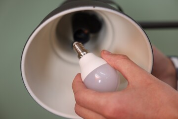 Wall Mural - Man changing light bulb in lamp on greyish green background, closeup