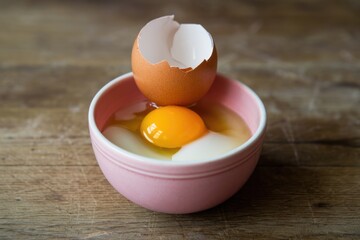 Poster - A cracked eggshell sits atop a pink bowl containing separated egg yolks and whites.