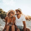 © bersch28 - A relaxed couple wearing summer hats sit laughing on the sandy beach as sunlight bathes them, exemplifying joy, relaxation, and a carefree beach lifestyle.