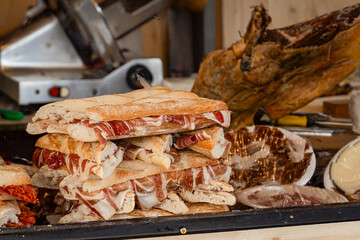 Canvas Print - Freshly made sandwiches featuring iberian ham are stacked and ready to be enjoyed at a bustling market stall