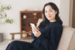 © lielos - リビングのソファーに座りながらスマートフォンの操作をする女性。