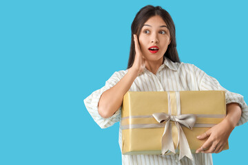 Wall Mural - Beautiful shocked Asian woman with gift box on blue background