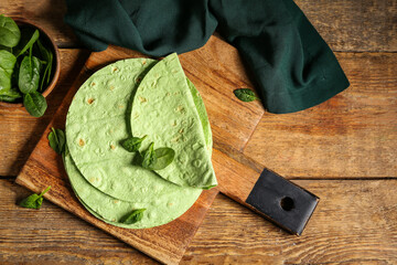 Wall Mural - Board with round green lavash and bowl of spinach on wooden background