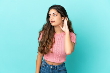 Young caucasian woman isolated on blue background listening to something by putting hand on the ear