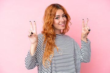 Wall Mural - young caucasian woman isolated on pink background showing victory sign with both hands