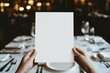 © Ace64 Studio - hand holdin a blank Menu paper luxury restaurant table with a plate and silver cutlery background blank mock up menu sheet
