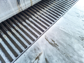 Wall Mural - Soap sud waste flows to floor drain grid in car washing garage, close-up.