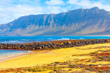 Wall Mural - Azure waters lap against volcanic shores, painting a breathtaking canvas. Majestic mountains meet the cerulean Atlantic Ocean at Famara Beach in Lanzarote, Canary Islands Spain