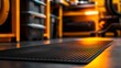 © Phatharaporn - Close up view of a black rubber floor mat with a textured surface, illuminated by warm orange light in a workshop. The background is blurred, showing shelves and tools.