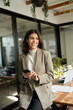 © Stock 4 You - 30s middle eastern business woman professional using mobile phone ai application for work. Smiling latin businesswoman it specialist standing in modern office, holding smartphone cellphone. Vertical