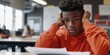 © Y_Malashkevych - A teenage boy is intently studying his exam paper in a well-lit classroom showing a pensive expression as he scratches his head unsure of the answers