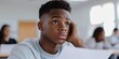 © Y_Malashkevych - In a bright classroom a 14-year-old African American boy scratches his head while looking at his exam paper displaying a thoughtful yet uncertain expression as he contemplates answers