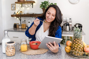 Wall Mural - young latin woman overweight using tablet while having breakfast at home kitchen in Mexico Latin America, hispanic plus size female	