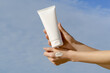 © Daryna  - Female hands with smear hold white mockup tube on blue sky background. Concept of beauty products, face and body care