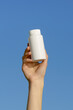 © Daryna  - Vertical image of a female hand holding a white mockup pill bottle on a blue isolated background. Concept of health, dietary supplements and vitamins. Image for your design