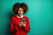 © Maryna - Young happy Latin woman use smartphone for online shopping. Attractive person smile while typing message. Casual attire. Bright teal background. Digital tech use. Woman shopping online.