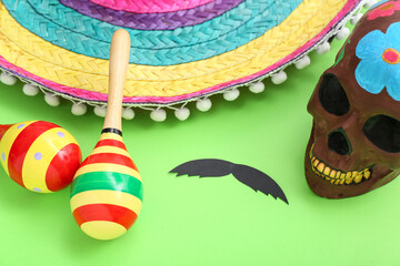 Wall Mural - Mexican maracas, paper mustache, painted skull and sombrero hat on green background, closeup