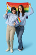 © Pixel-Shot - Young lesbian couple with LGBT flags showing victory gesture on blue background