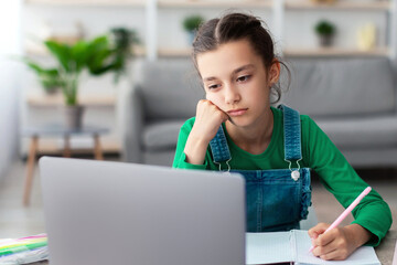 Aufkleber - Too Tired For School. Portrait of bored upset student girl sitting at desk, doing homework, writing in her notebook and looking at laptop screen, studying online, selective focus. Home Based Learning