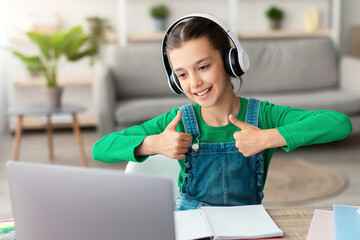 Poster - Smiling girl in headphones enjoying elearning sitting at table showing thumbs up to pc webcam, recommending e-study and online school for children, using modern tech. Clever kid, homeschooling concept