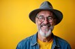 © Maryna - Happy senior man with hat, glasses smiles broadly against bright yellow background. Gray beard, wearing denim jacket over yellow shirt. Photo conveys happiness, style in modern way. Photo portrait