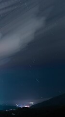 Wall Mural - starry sky with clouds and city lights bellow, time lapse vertical view