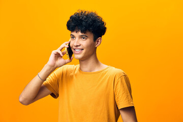 Wall Mural - Young man talking on the phone, smiling against a vibrant yellow background, casual attire, positive energy, communication and happiness captured in the moment