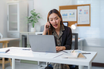 Asian businesswoman talking on phone and working on laptop in modern office