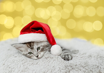 Poster - Cozy Maine coon kitten wearing red santa hat lying on festive background. Empty space for text