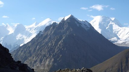 Wall Mural - View of the marble wall and Khan Tengri peak. Snowy peaks partially covered with clouds. Steep cliffs of high mountains. The gorge. The border of three countries. An ancient snow glacier.