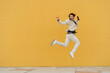 © Westend61 - Businessman jumping in the air in front of yellow wall listening music with headphones and smartphone