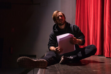 Actor sitting on stage of theatre with script