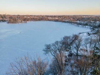 Wall Mural - Serene winter landscape of a frozen lake surrounded by bare trees and distant houses. New York